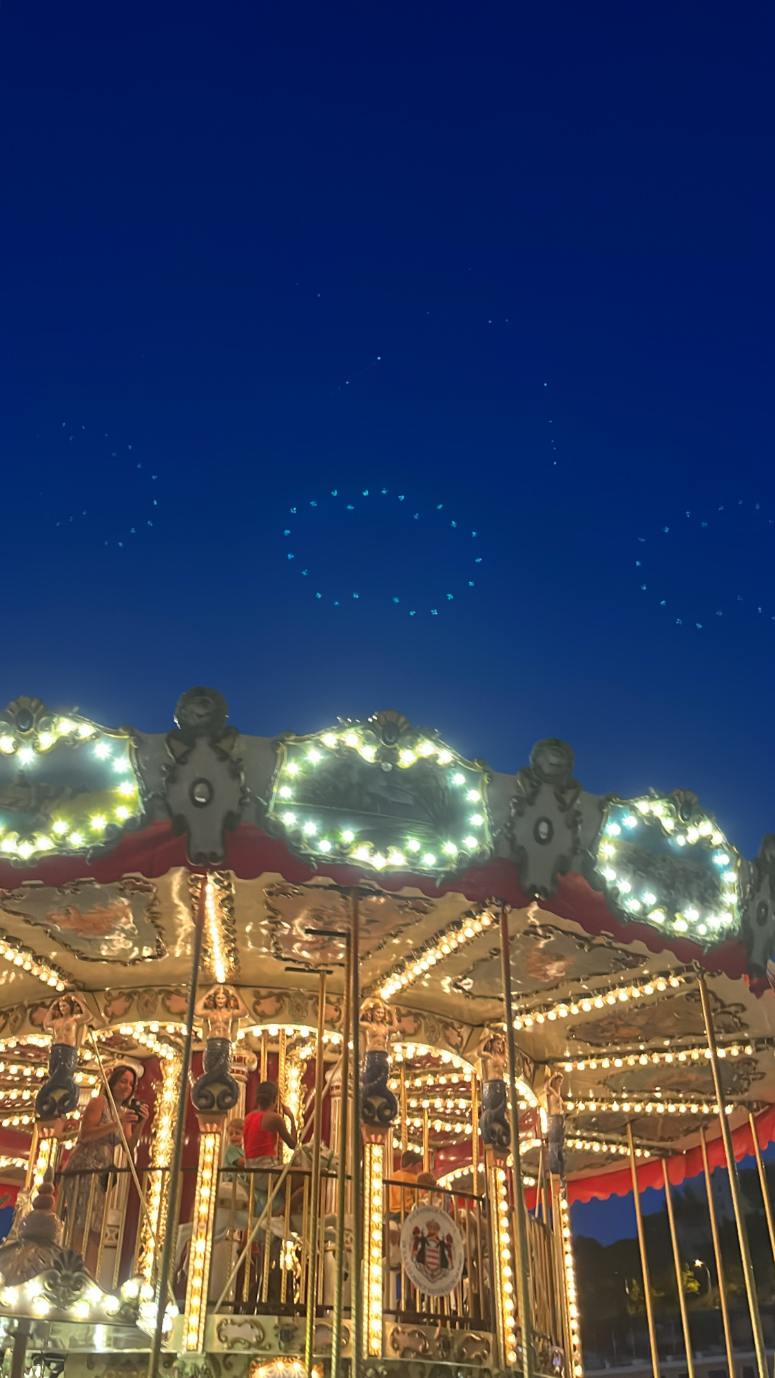 Din Tanovic — vintage carousel glowing under deep blue Monaco sky with drone-show stars