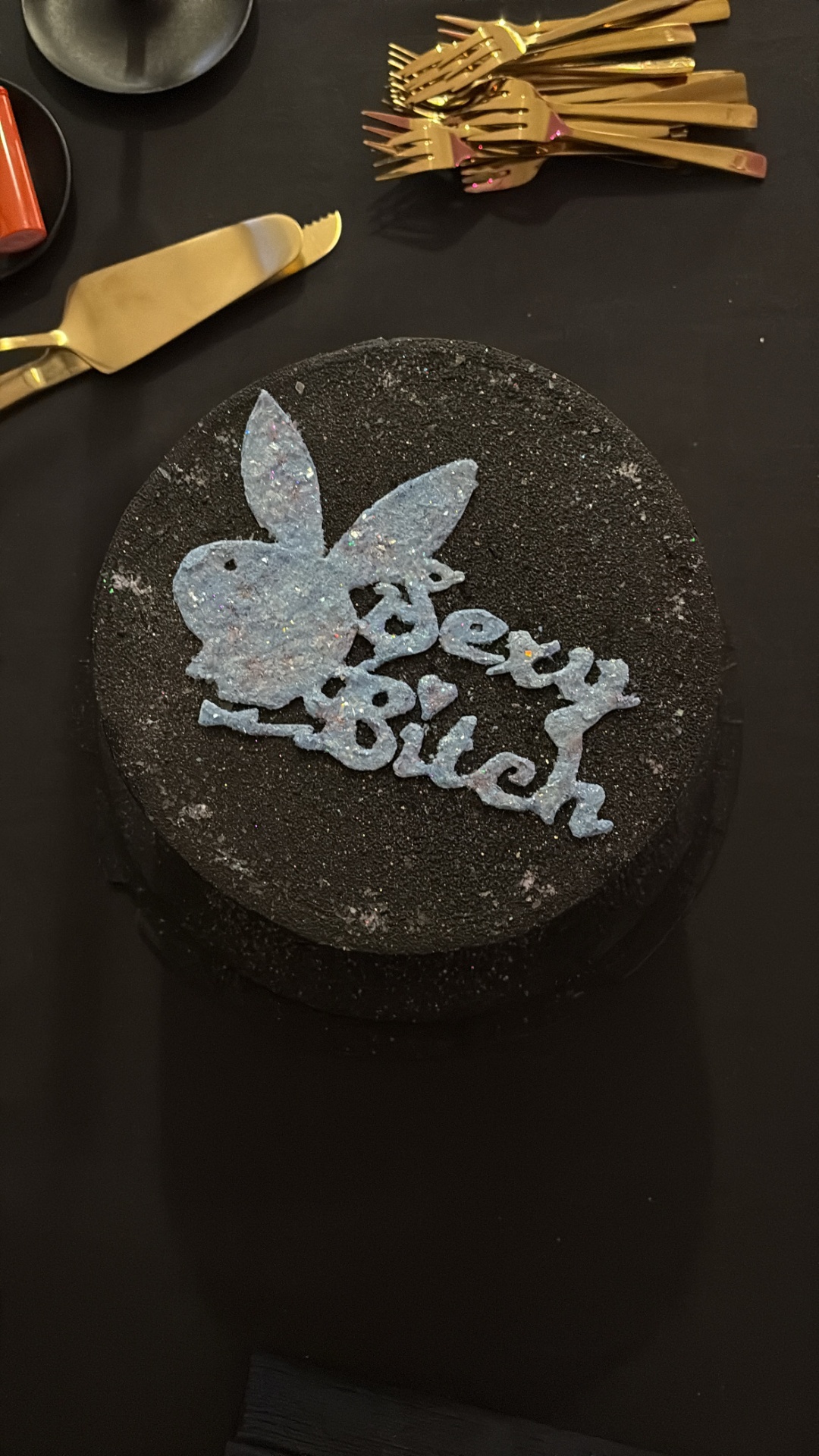 Din Tanovic — black 'Sexy Bitch' birthday cake with gold cutlery on a dark table in Stockholm
