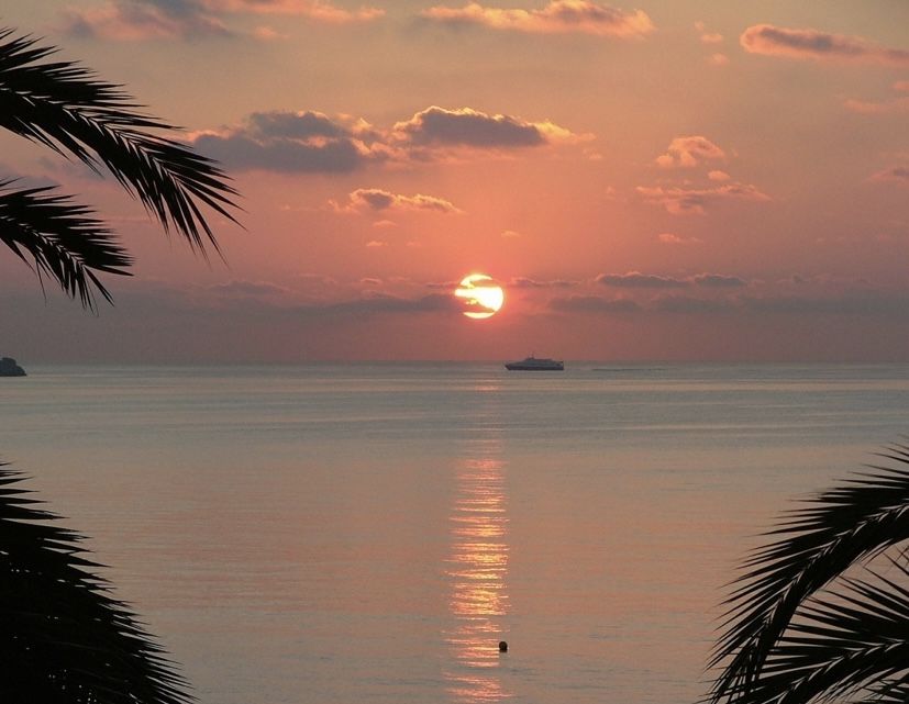 A small ferry crossing a coral-colored sunset — from Din Tanovic's travel mood collection